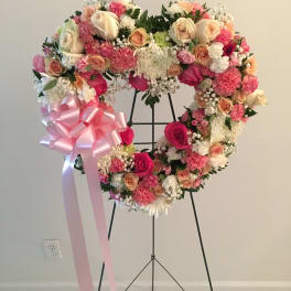 Heart-shaped floral wreath with pink and cream roses and a large pink ribbon