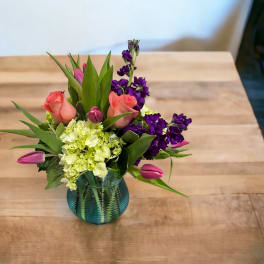 Pink roses and purple flowers arranged in a blue glass vase