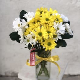 Bouquet of yellow and white daisies in a glass vase with a yellow ribbon