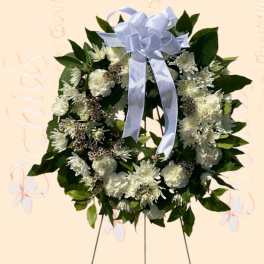 White floral wreath with a pale blue ribbon bow on a stand