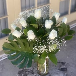 White roses in a glass vase with baby's breath and large tropical leaves