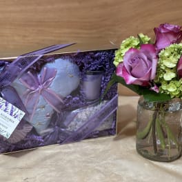 Pink roses and green hydrangeas in a glass jar beside a lavender gift set