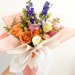 Hand-tied bouquet of orange, white, pink, and blue flowers in pastel wrapping