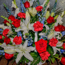 Red roses, white lilies, and blue flowers in a basket arrangement