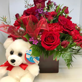Red rose bouquet with a white teddy bear and ribbon in a square vase