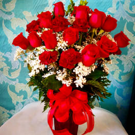 Red roses and carnations arranged in a vase with a red ribbon