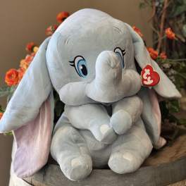 Plush gray elephant toy sitting in a wooden barrel with orange flowers behind it