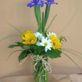 Yellow and white daisies with purple irises in a glass vase