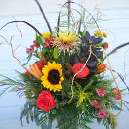 Tall mixed bouquet with sunflowers, red roses, and pink alstroemeria in a glass vase