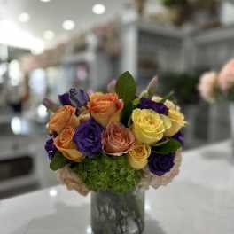 Mixed roses in orange, yellow, purple, and pink in a glass vase
