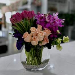 Bouquet of peach roses, purple tulips, and magenta orchids in a glass vase