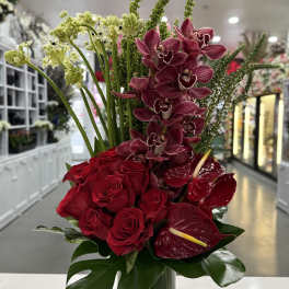 Red roses and burgundy orchids in a tall glass vase