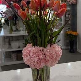 Pink hydrangeas with orange tulips in a clear square vase