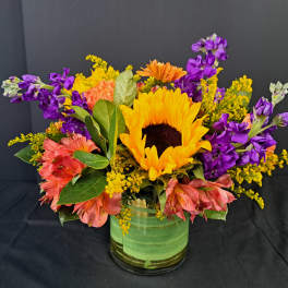 Sunflower bouquet with purple and pink flowers in a green glass vase