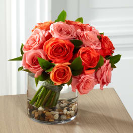 Bouquet of pink and coral roses in a glass vase with pebbles