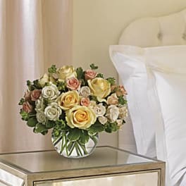 Bouquet of pastel roses in a clear glass vase on a bedside table