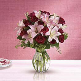 Bouquet of pink lilies and red roses in a clear glass vase