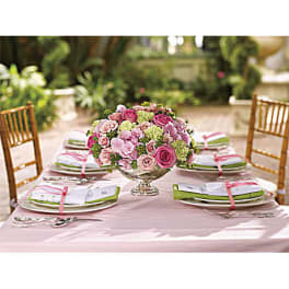 Pink and green floral centerpiece on a table set with plates and napkins