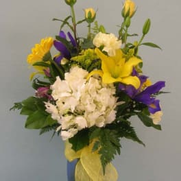 Yellow and purple mixed flower arrangement in a blue vase with a yellow ribbon