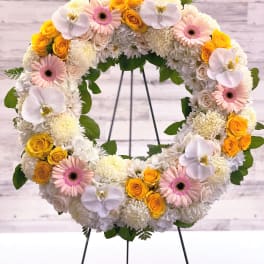 Circular floral wreath with white, pink, and yellow blooms on a stand