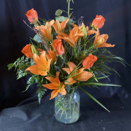 Orange roses and lilies arranged in a clear glass vase