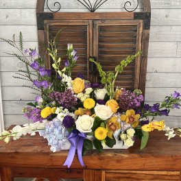 Mixed flower arrangement with roses, orchids, and purple blooms in a white container