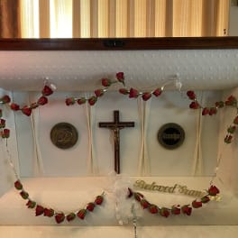 White casket with red rose garland and a crucifix inside