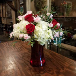 Bouquet of red roses, white hydrangeas, and pink carnations in a red glass vase