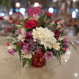 Mixed pink, white, and purple flowers in a red heart-patterned container