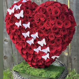 Heart-shaped arrangement of red roses with white butterflies on a moss-covered base