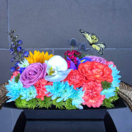 Colorful mixed flower arrangement in a black rectangular container with butterfly picks