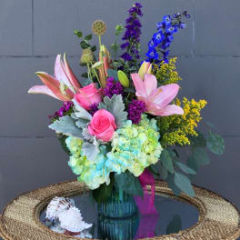 Colorful bouquet of lilies, roses, hydrangeas, and delphinium in a glass vase