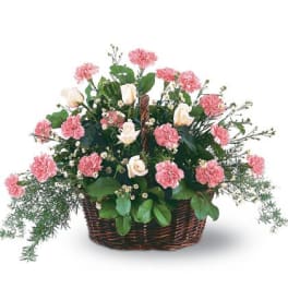 Pink carnations and white roses arranged in a brown wicker basket.