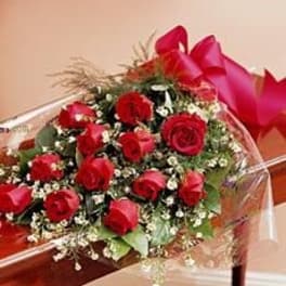 Spray-style bouquet of red roses with white filler flowers wrapped in cellophane and tied with a red bow