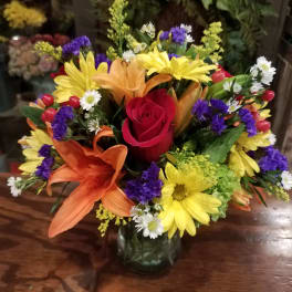 Mixed bouquet with a red rose, lilies, and yellow daisies in a glass vase