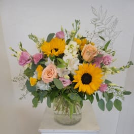 Mixed bouquet with sunflowers, roses, and white blooms in a glass vase