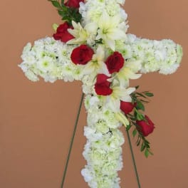 Cross-shaped floral tribute with white flowers and red roses on a stand