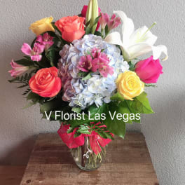 Bright mixed bouquet of roses, lilies, hydrangea and alstroemeria in a clear glass vase on a wooden crate.