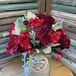 Red floral arrangement in a metal container with a heart label