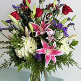Bouquet of pink lilies, red roses, and white hydrangeas in a glass vase