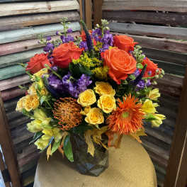 Colorful mixed bouquet with roses, purple blooms, and orange gerbera daisies in a vase
