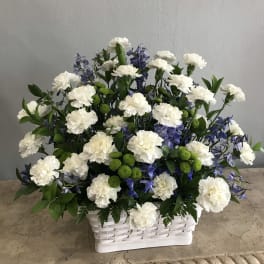 White carnations and blue flowers arranged in a white basket