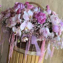 Pink floral arrangement in a wicker basket with orchids and peonies