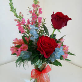 Bouquet of red roses and pink snapdragons in a glass vase with a red ribbon