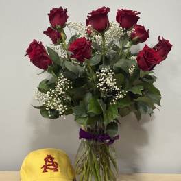 Bouquet of red roses in a glass vase with a yellow cap beside it.