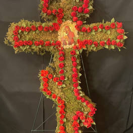 Cross-shaped floral tribute with red roses and a religious icon in the center