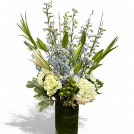 Tall white and pale blue floral arrangement in a dark glass vase