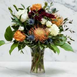 Bouquet of orange, white, and burgundy flowers in a clear glass vase
