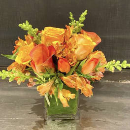 Orange and yellow floral arrangement in a square glass vase