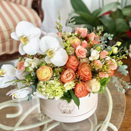 Peach roses and white orchids arranged in a round white box
